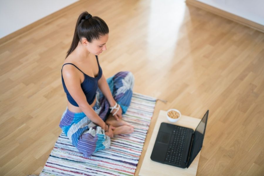 Femme pratiquant une méditation guidée en ligne sur tapis de yoga avec ordinateur portable
